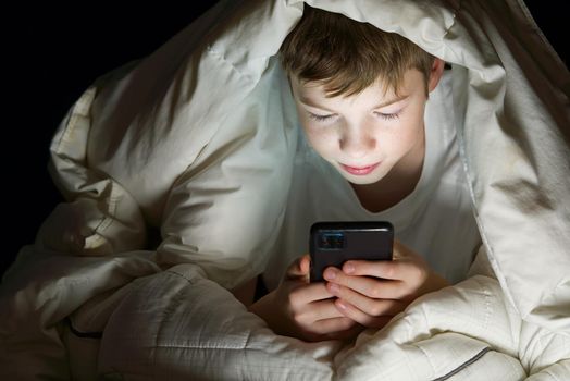 Social media addiction Boy hiding under the blanket at night in his bed communicates on Internet. Child gadget addiction and insomnia. lonely boy using smartphone at night in bed