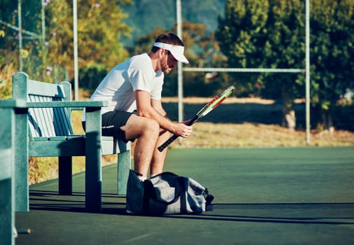 Shot of a sporty young man sitting on a bench on a tennis court