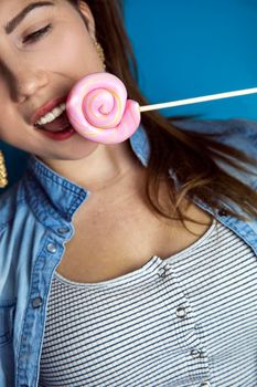 Portrait of a beautiful girl with colorful pink twirl lollipop hard candy on blue background, sweets,sugar and unhealthy food concept beauty