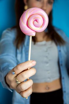 Happy beautiful woman giving colorful pink twirl lollipop on light blue background. Sweets,hard candy,gift,present concept sugar