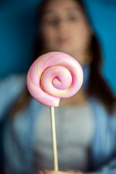 Happy beautiful woman giving colorful pink twirl lollipop on light blue background. Sweets,hard candy,gift,present concept sugar