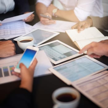 Closeup shot of a group of professionals using different devices while sitting together at a table in an office