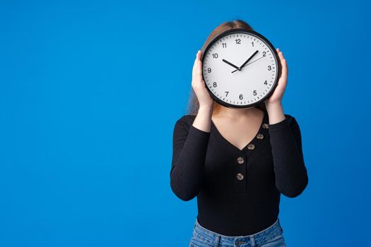 Beautiful teen girl holding wall clock over blue background, close up