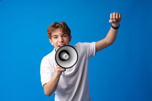 Teen boy making loud announcement against blue background, close up