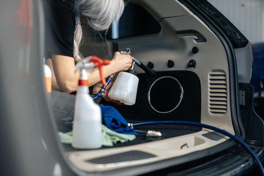 Woman cleaning car salon with polishing spray in car detailing service, close up