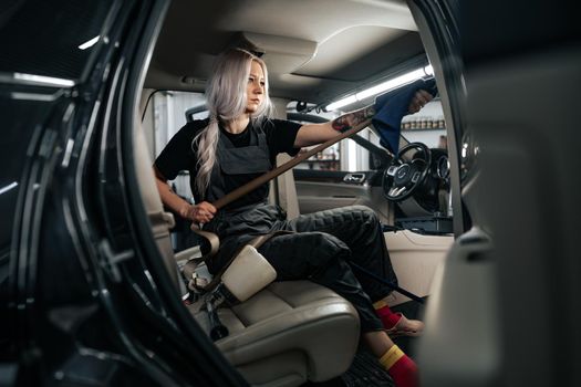 Woman cleaning car salon with polishing spray in car detailing service, close up