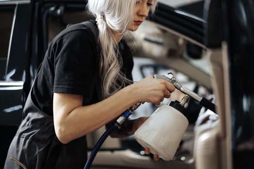 Woman cleaning car salon with polishing spray in car detailing service, close up