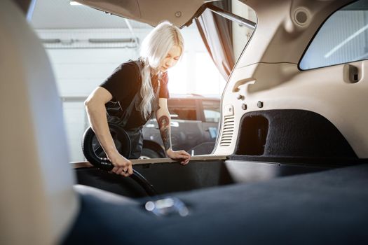 Worker woman vacuum cleaning dust interior inside car in car wash, close up