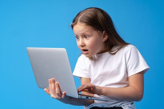 Portrait of a little girl holding laptop computer while standing against blue background, close up