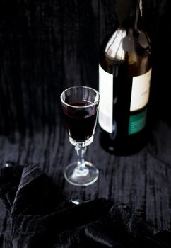 bottle and a glass of red wine on a black background