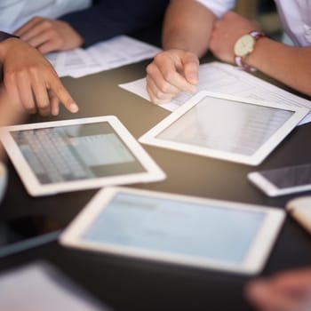 Closeup shot of a group of professionals using different devices while sitting together at a table in an office