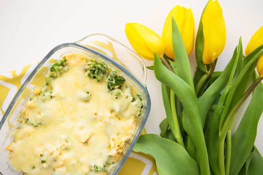 casserole with broccoli, cheese and cream on a background of yellow tulips