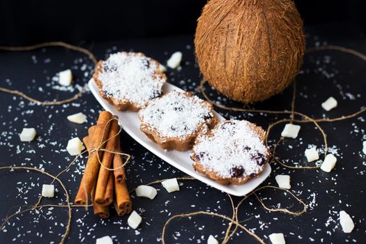 coconut muffins on a black background with cinnamon sticks and whole coconut