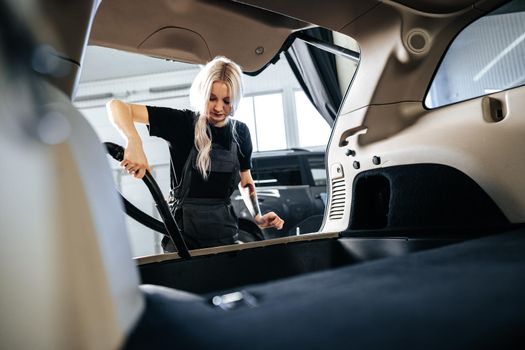 Worker woman vacuum cleaning dust interior inside car in car wash, close up
