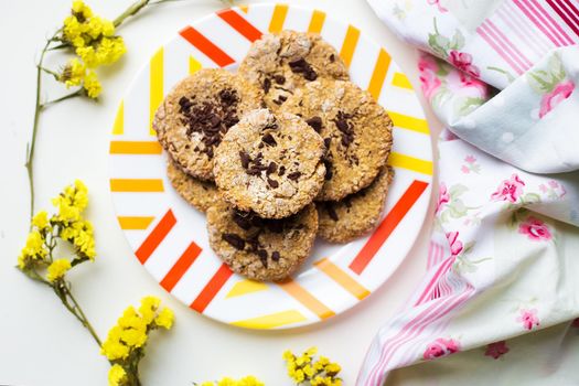 Oatmeal cookies with chocolate on a plate with bright cloth and flowers