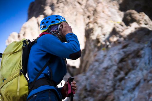 A young man with climbing equipment, a helmet, an assault backpack climbs among the snow-capped rocky mountains along a trail to the top, a tourist is engaged in mountaineering.