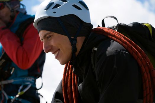 Two young hikers go mountaineering. Happy traveler in a helmet, with a rope, climbing equipment, backpack climbs to the top of a snow-capped mountain with a friend.