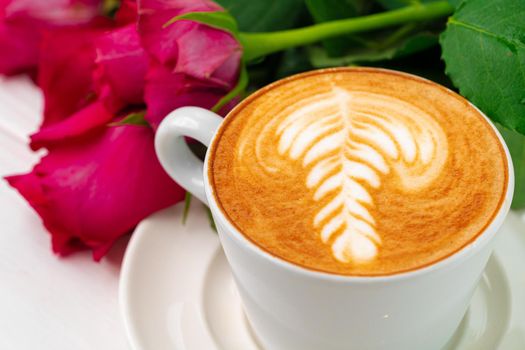 Cup of cappucino with art and bouquet of roses on wooden table close up