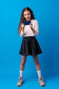 Little girl using mobile phone.against blue background, close up