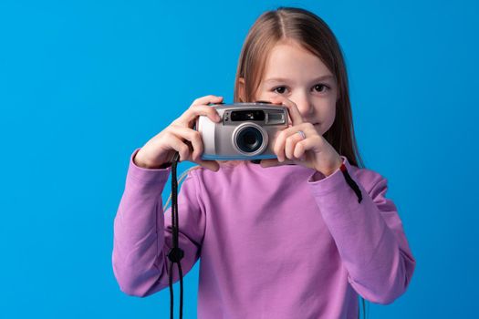 Portrait of a little girl with camera against blue background, close up