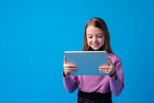 Little girl uses a digital tablet on a blue background, close up
