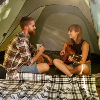 Shot of a young woman playing guitar to her boyfriend in a tent