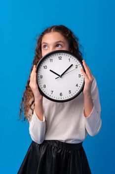 Beautiful teen girl holding wall clock over blue background, close up