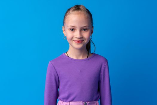 Portrait of a little smiling girl preteen on blue background, close up