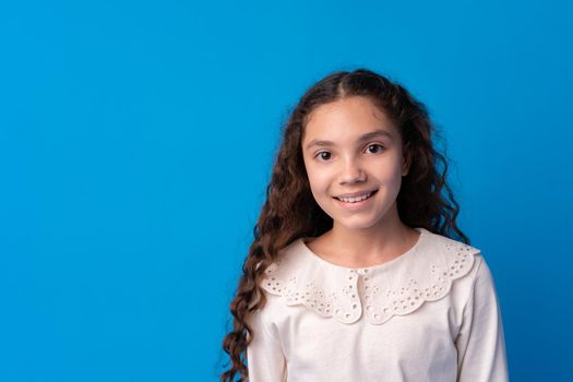 Portrait of a little smiling girl preteen on blue background, close up