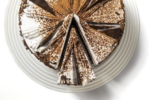 cake with chocolate, sprinkled with chocolate chips, on a tray on a white background with a cut piece. top view.