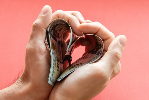several 100 dollar bills folded in the shape of a heart in male hands. love of money, greed, business, wealth.