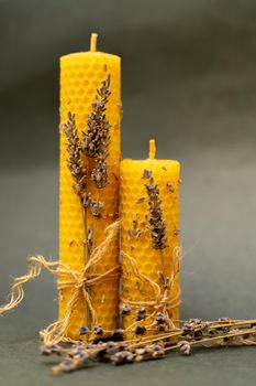 Two beeswax candles on a gray background. The candles are decorated with sprigs of lavender and tied with a jute rope