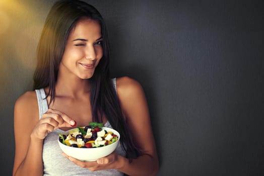 Portrait of a healthy young woman eating a salad against a gray background