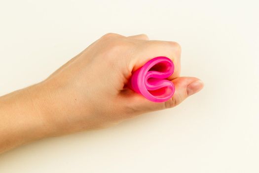 Female hand holding a pink Menstrual Cup folded with a C-Fold Method. Folding Menstrual Cup is for comfortable inserting it into vagina to collect blood during woman periods