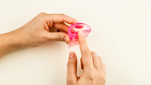 Female hands folding a Silicone Menstrual Cup over beige Background. Sanitary Tool for Comfortable and Zero Waste Woman Cycle Period