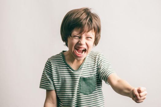Angry kid shouting and rising his fist. Aggressive little boy with mouth wide open looking to the camera. ADHD syndrome