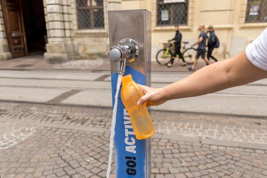 Graz, Austria - August 23, 2021: Woman refilling her water bottle with fresh Drinking Water in a public tap fountain in the downtown of Graz