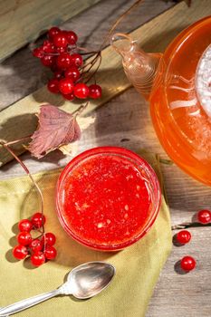 Viburnum jam in a glass bowl on the rustic style wooden table with a hot winter drink and viburnum berries
