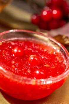 Viburnum jam in a glass bowl on the rustic style wooden table with a hot winter drink and viburnum berries