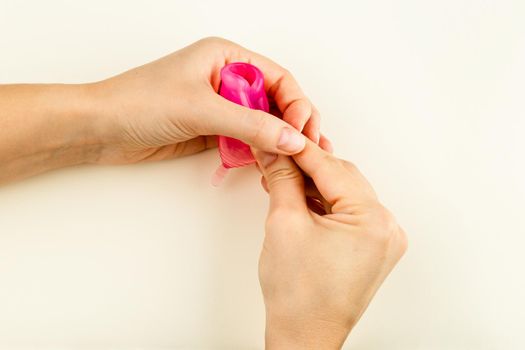 Female hands showing how to use a Menstrual Cup by folding it with a Punch-Down Method. Silicone Menstrual Cup inserts into vagina to collect blood during Woman Menstruation