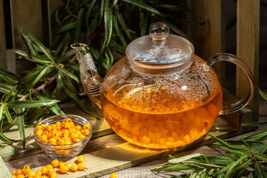 Hot winter drink made from Sea Buckthorn berries in a glass kettle on wooden table