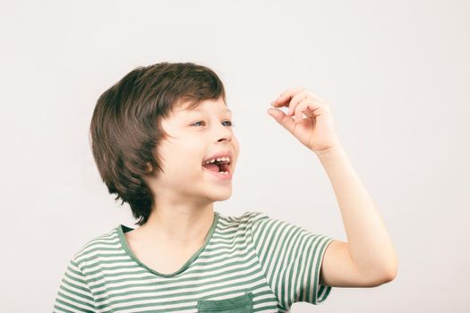 Cheerful boy looking at his first lost bottom front milk tooth over grey background. Child dental health care concept.