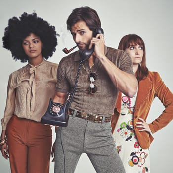 Two attractive young hippies standing behind a handsome man using a retro telephone