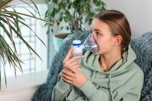 Teenage girl makes inhalation with a nebulizer equipment. Sick child holding inhalator in hand and breathes through an inhaler at home. Physical therapy for cold, flu and bronchial asthma