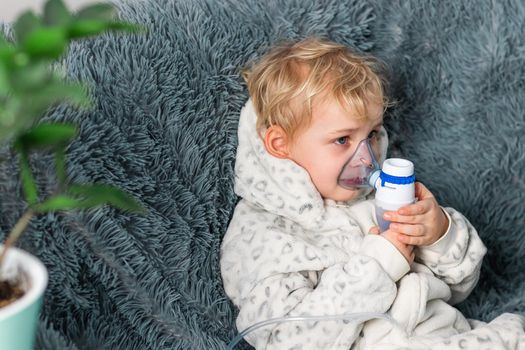 Cute baby boy makes inhalation with a nebulizer equipment. Sick child holding inhalator in hand and breathes through an inhaler at home. Physical therapy for cold, flu and bronchial asthma