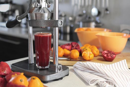 glass of freshly squeezed pomegranate juice, chopped pomegranates, tangerines and a pomegranate juicer at home.