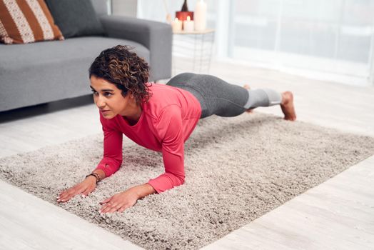 Full length shot of an attractive young woman exercising and holding a plank while in her living room at home