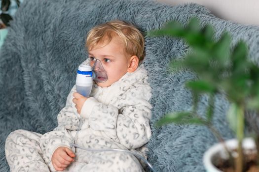 Cute baby boy makes inhalation with a nebulizer equipment. Sick child holding inhalator in hand and breathes through an inhaler at home. Physical therapy for cold, flu and bronchial asthma