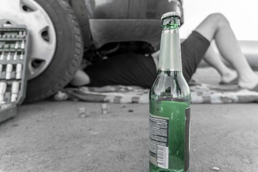 Alcohol and Car repairs.A drunk person lies under the car repairing it and conducting an inspection and analysis of the breakdown.A bottle of beer by the car in close-up. An auto mechanic in a car