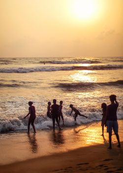 Kalutara, Sri Lanka - April 15, 2017: Silhouettes of people, mostly children playing on the beach, sea and golden sunset afternoon light in background.